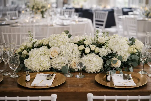 Centro de mesa alargado de hortensias y rosas blancas con platos base dorados