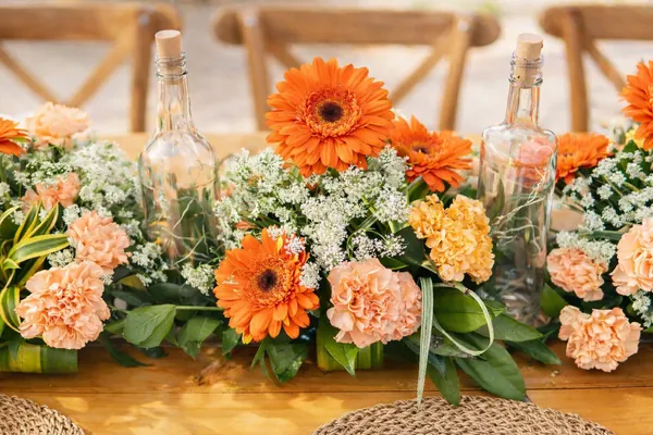 Centro de mesa alargado de gerberas naranjas, claveles melocotón y flores blancas