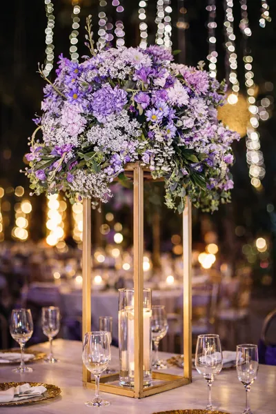 Centro de mesa alto de flores lilas y blancas sobre una base dorada