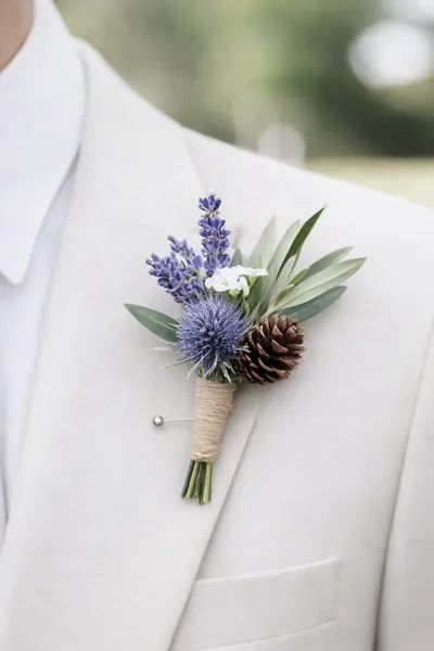 Boutonnière de lavanda, cardo y piña atado con yute en un traje marfil