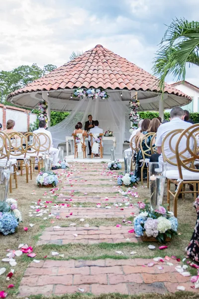Pasillo de ceremonia al aire libre con pétalos y arreglos florales junto a las sillas